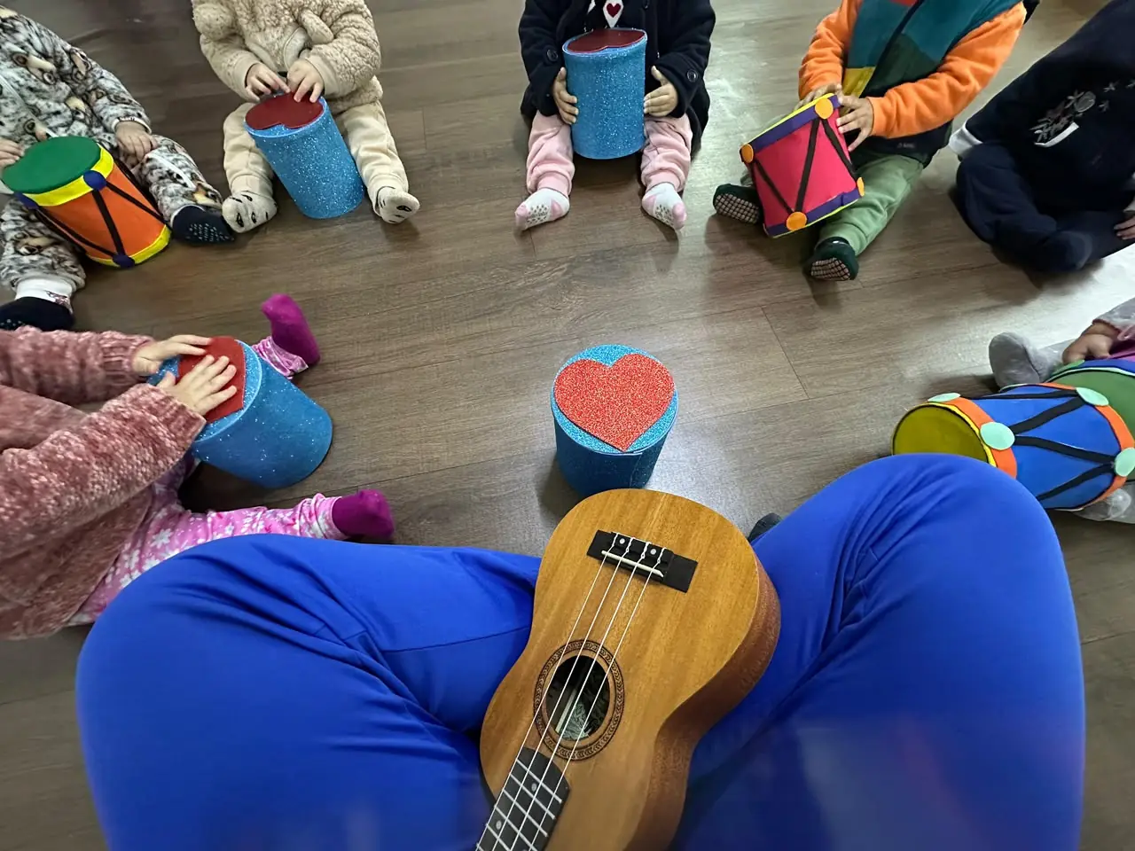 Roda de crianças com tambores artesanais e ukulele no centro